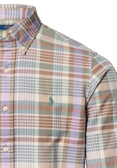 Chemise à carreaux en coton, avec des teintes de marron, de vert et de violet. Logo brodé sur la poitrine. Col classique et patte de boutonnage.