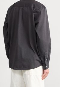 Camicia nera con bottoni in cotone liscio, caratterizzata da maniche lunghe, pince sul retro e polsini con un solo bottone.