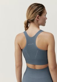 Grå sportbh med racerback-design och dekorativa perforeringar på baksidan. Tillverkad av ett mjukt, elastiskt tyg för komfort och flexibilitet.