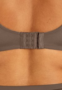 Brun behåbandsslutning med hak-och-öga-design och flera justeringsalternativ, som visar en slät textur och stretchigt tyg.