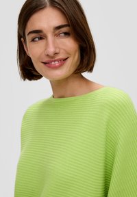 Grüner gerippter Pullover mit lockerer Passform und Bootsausschnitt, der einen strukturierten Stoff aufweist, der Tiefe und Dimension verleiht.