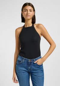 Svart ribbad halterneck-topp med en åtsittande design, matchad med blå denimjeans. Toppen har en diskret logotyp på bröstet.