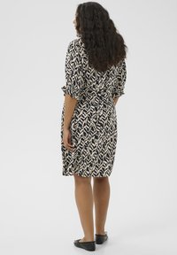 Black and cream patterned dress with short sleeves, belted at the waist, knee-length, paired with black flats.