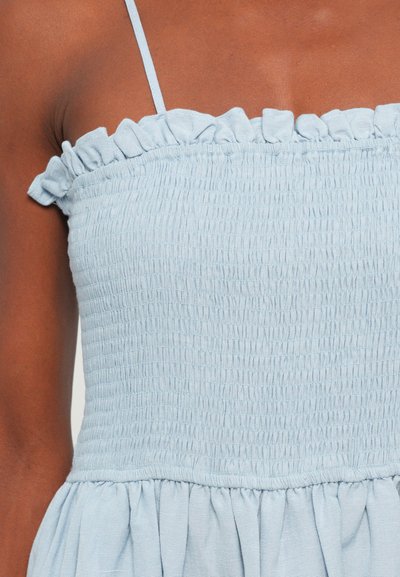  Lichtblauw mouwloos topje met smock-textuur, gedrapeerde halslijn en een uitlopende onderrand. Soepele, lichtgewicht stof.