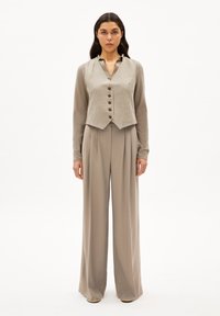 Beige Weste mit Nadelstreifen und fünf braunen Knöpfen, kombiniert mit hoch taillierten, weit geschnittenen Hosen aus passendem beigem Stoff. Glatte Textur.