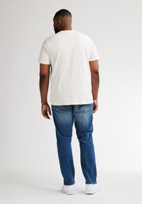 Camiseta blanca de algodón con mangas cortas, combinada con jeans de mezclilla azul. Los jeans presentan un ligero efecto degradado y tienen un corte relajado.