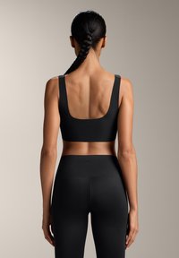 Črn športni modrček z širokimi naramnicami in izrezom na hrbtu, izdelan iz gladkega materiala. V kombinaciji z visokim črnim leggingom, ki ima brezšivno zasnovo.