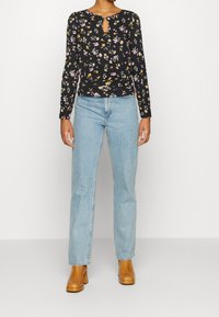 Svart långärmad topp med flerfärgad blommönster och en nyckelhålsk neckline, i kombination med ljusblå raka jeans och bruna klackstövlar.