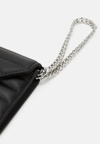 Czarna skórzana kopertówka o pikowanym wzorze, z metalowym łańcuszkiem i zapięciem na klapkę. Kompaktowy i elegancki design z minimalistycznymi detalami.