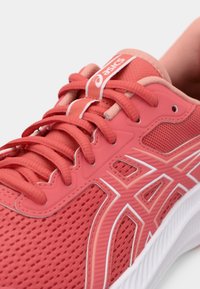 Chaussure de sport rose avec une tige en maille, des motifs texturés, des accents blancs et une languette rembourrée avec des lacets pour un maintien sécurisé.
