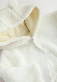 Weißer Fleece-Schlafanzug mit einer weichen, plüschigen Textur, ausgestattet mit einer Kapuze und Pompon-Detail. Innen hat er ein glattes, leichteres Stofffutter.