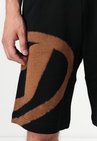 Black shorts featuring a large, abstract brown pattern. Made of soft fabric, with a smooth texture and a standard hemline.