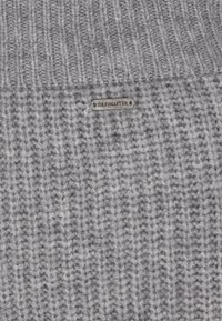 Grauer Strickpullover mit gerippter Textur, ausgestattet mit einem kleinen Metalletikett, auf dem "DREIMASTER" steht, das in den Stoff genäht ist.