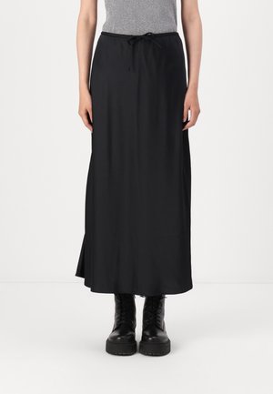 Kobieta ubrana w długą czarną spódnicę z sznurkiem w talii oraz czarne sznurowane buty wojskowe, w połączeniu z szarym topem bez rękawów.