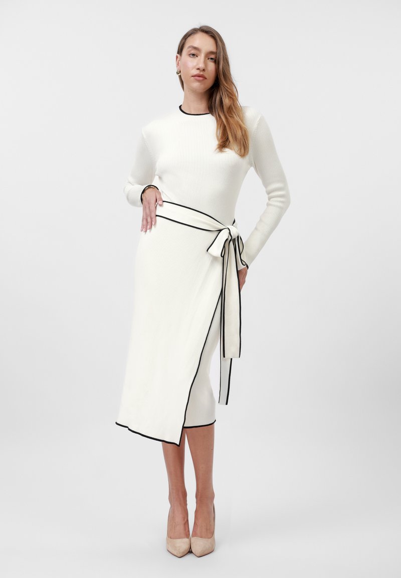 Knit dress in off-white with black trim, featuring a wrap design and tied belt accent at the waist. Long sleeves and fitted silhouette.