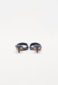 Sandales à talons bleu marine avec un dos ouvert courbé, présentant un motif géométrique en bleu clair et un talon slim et effilé.