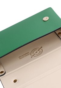 Portafoglio in pelle verde con finitura liscia, dotato di chiusura a scatto dorato e interno crema. Testo impresso che recita "Made in Italy."