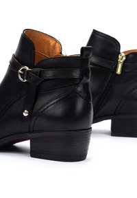 Bottines en cuir noir avec un talon bas, dotées d'une sangle réglable, de quincaillerie en ton doré et d'une fermeture éclair sur le côté pour un enfilage facile.