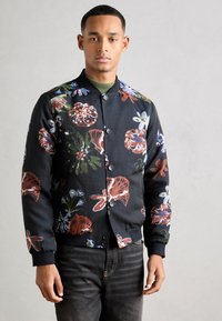 Λουλουδάτο bomber jacket με μαύρο φόντο, έντονα πολυχρωμα λουλούδια, ριμπ μανσέτες και κουμπωτή κλείσιμο. Συνδυασμένο με σκούρες τζιν.