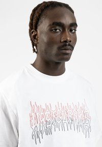White cotton t-shirt featuring red and black flame-like text graphic on the front. Short sleeves and crew neckline, smooth texture.
