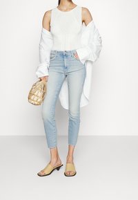 Body blanco de canalé con un patrón sutil, jeans de tiro alto azul claro con dobladillo deshilachado y zuecos amarillos de tacón bajo.