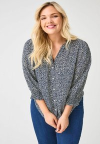 Blouse marine à imprimé léopard blanc, manches longues avec poignets froncés, fermeture à boutons, coupe décontractée, associée à un jean en denim bleu.