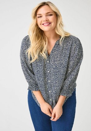 Navy blouse with white leopard print, long sleeves with gathered cuffs, button closure, relaxed fit, paired with blue denim jeans.