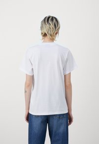 Hvid bomulds t-shirt med korte ærmer, afslappet pasform, rund halsudskæring og ingen synlig branding. Bæres med blå, løstsiddende denim jeans.