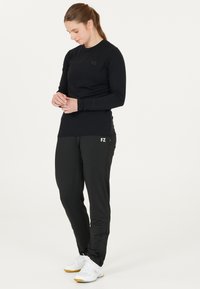 Svart långärmad träningsskjorta med FZ-logotyp; i kombination med svarta träningbyxor med en zipficka och vit FZ-logotyp, bärs tillsammans med vita sneakers.