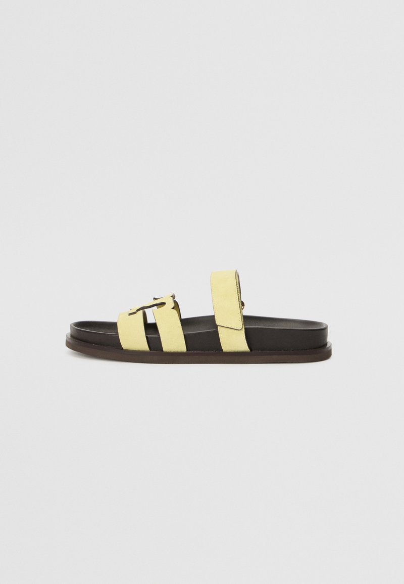 Sandálias de slide amarelas em camurça com duas correias, fivela ajustável e sola de borracha castanha escura. Textura suave com um design minimalista.
