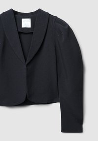 Blazer nero cropped con spalle strutturate, motivo a pois sottile e tessuto liscio. Nota il rever anteriore e la chiusura a un bottone.
