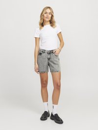 Model nosi belo kratko majico s kratkimi rokavi, sivo denim kratke hlače, bele nogavice in črne loaferje. Obleka ima sproščen kroj in vsakdanji slog.