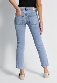 Jeans de mezclilla azul claro con pierna recta, que cuentan con dos bolsillos traseros y una etiqueta en la cintura. La tela tiene una textura suave y ligeramente desgastada.