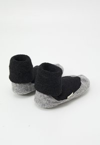 Zapatillas de fieltro gris y negras con un diseño bajo en el tobillo, parte superior texturizada y suela blanda, que cuentan con una pequeña etiqueta en un lado.