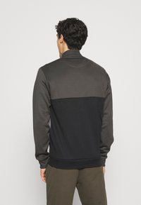 Sudadera negra y gris oscuro con un cuello alto, que presenta una textura suave, puños acanalados y un diseño de bloques de color en la parte posterior.