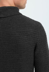 Maglione lavorato a maglia grigio scuro con un motivo testurizzato e colletto alto, realizzato in tessuto a trama stretta, visto da dietro.
