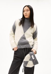 Pullover aus weichem Wollgemisch mit grauem und cremefarbenem Rautenmuster, Stehkragen und lockerer Passform. Kombiniert mit dunklen Hosen und einer passenden Mütze.