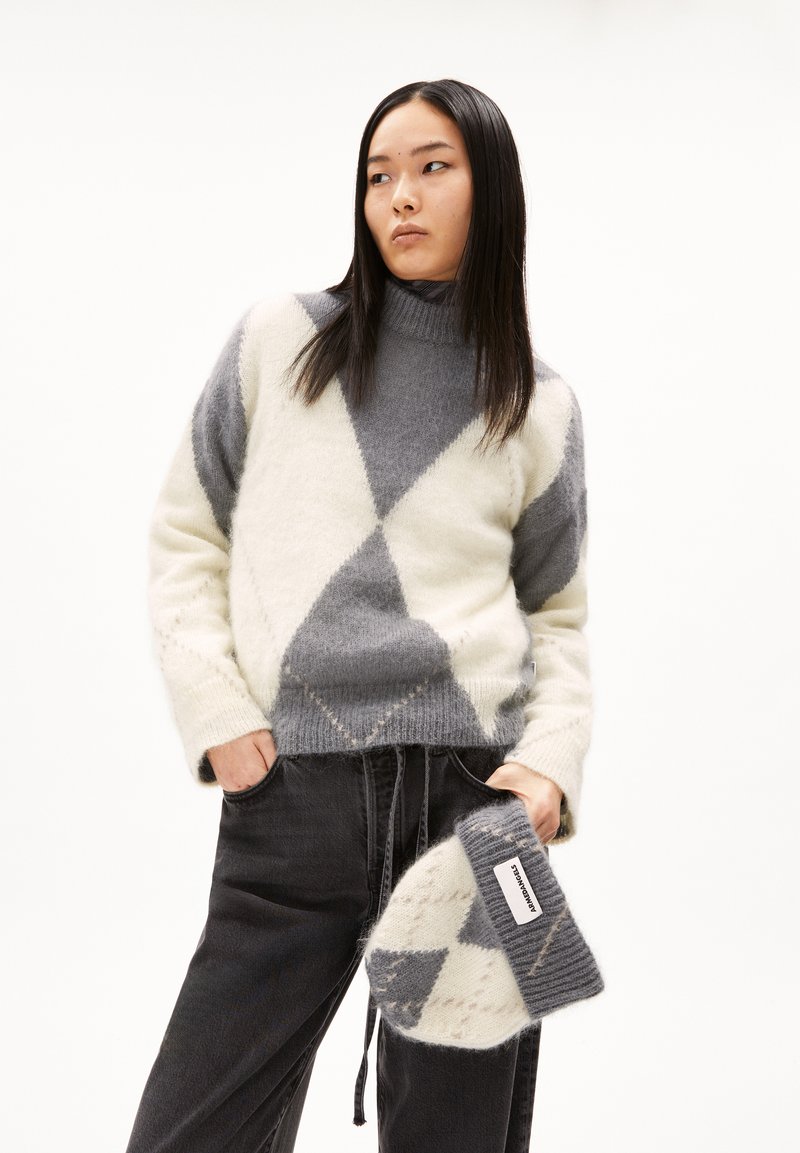 Pullover aus weichem Wollgemisch mit grauem und cremefarbenem Rautenmuster, Stehkragen und lockerer Passform. Kombiniert mit dunklen Hosen und einer passenden Mütze.