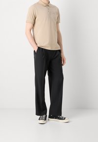 Beige polo shirt med korte ærmer og krave, parret med sorte plisserede bukser og sorte sneakers med hvide såler.