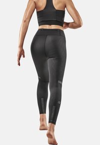 Leggings de sport noirs avec un motif texturé en losanges, taille haute et accents réfléchissants. Fabriqués dans un matériau extensible, conçus pour le mouvement.