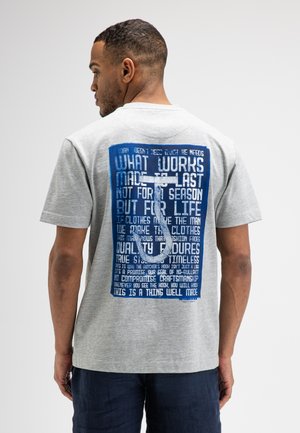 Mann trägt graues T-Shirt mit großem blauem Grafik- und Textdruck auf dem Rücken mit weißem Metzgerhaken-Design.