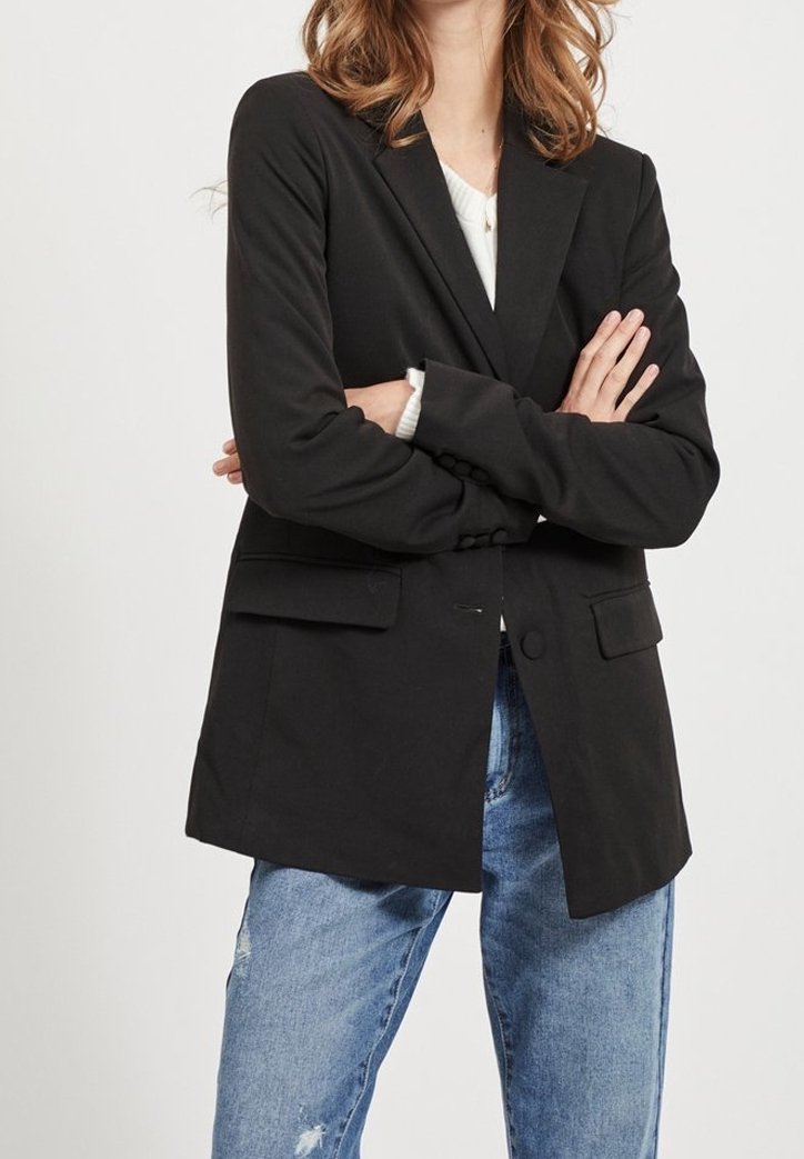 Blazer noir à coupe cintrée, fermeture à un bouton, col cranté et deux poches avant, associé à un jean délavé bleu clair et déchiré.