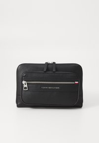 Černá kožená peněženka s texturovaným povrchem, vybavená centrálním zipovým oddílem a přední kapsou na zip. Minimalistický design, označený značkou "Tommy Hilfiger."