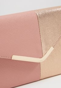 Dvoudílný psaníčko s matnou růžovou částí a třpytivou zlatou částí. Zlaté kovové doplňky podél švu. Texturovaný povrch.