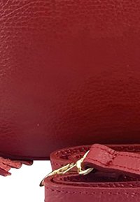 Rote Lederhandtasche mit strukturiertem Finish, ausgestattet mit einem abnehmbaren Trageriemen und goldenen Hardware-Akzenten. Abgerundete Form ohne sichtbare Muster.