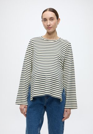 Bluză de maternitate cu mâneci lungi, cu dungi în culorile crem și bleumarin, având tiv curbat, deschizături laterale și croi lejer. Asortată cu blugi albaștri.