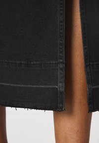 Fustă din denim negră cu margine brută, având o croială dreaptă și ușoare uzuri pe margini. Textură netedă, detalii de cusătură minime.