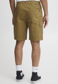 Khaki cargo shorts med flere lommer, elastisk liv, og rett snitt. Brukt sammen med svarte høyhælte sneakers og hvite sokker.