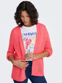 Coral knit cardigan with open front, three-quarter sleeves, and ribbed trim. Worn over a white graphic t-shirt with colorful designs.
