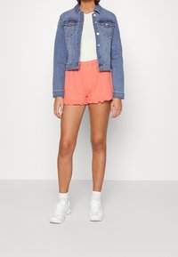 Jeansjacka med knappstängning, blå färg; vit T-shirt; korallfärgade shorts med scallopdetalj; vita sneakers. Enkelt, avslappnat outfit.